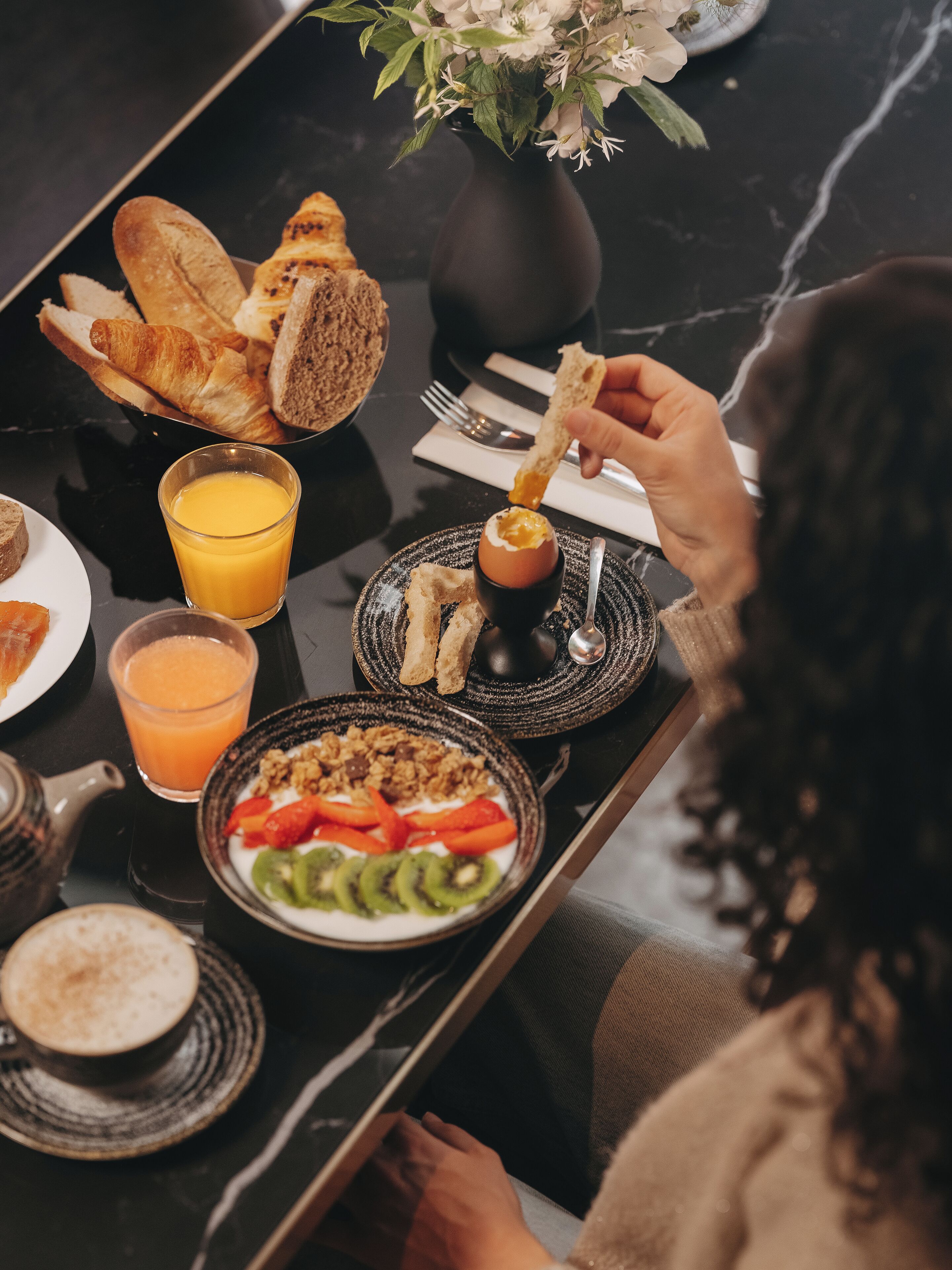 Una mesa de comedor con alimentos para el desayuno, incluyendo pan, una bebida caliente y una ensalada de frutas.