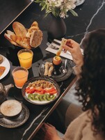 Una mesa de comedor con alimentos para el desayuno, incluyendo pan, una bebida caliente y una ensalada de frutas.