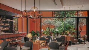 Un intérieur moderne avec des tables rondes, des chaises, un coin bar et de grandes fenêtres donnant sur un espace verdoyant.