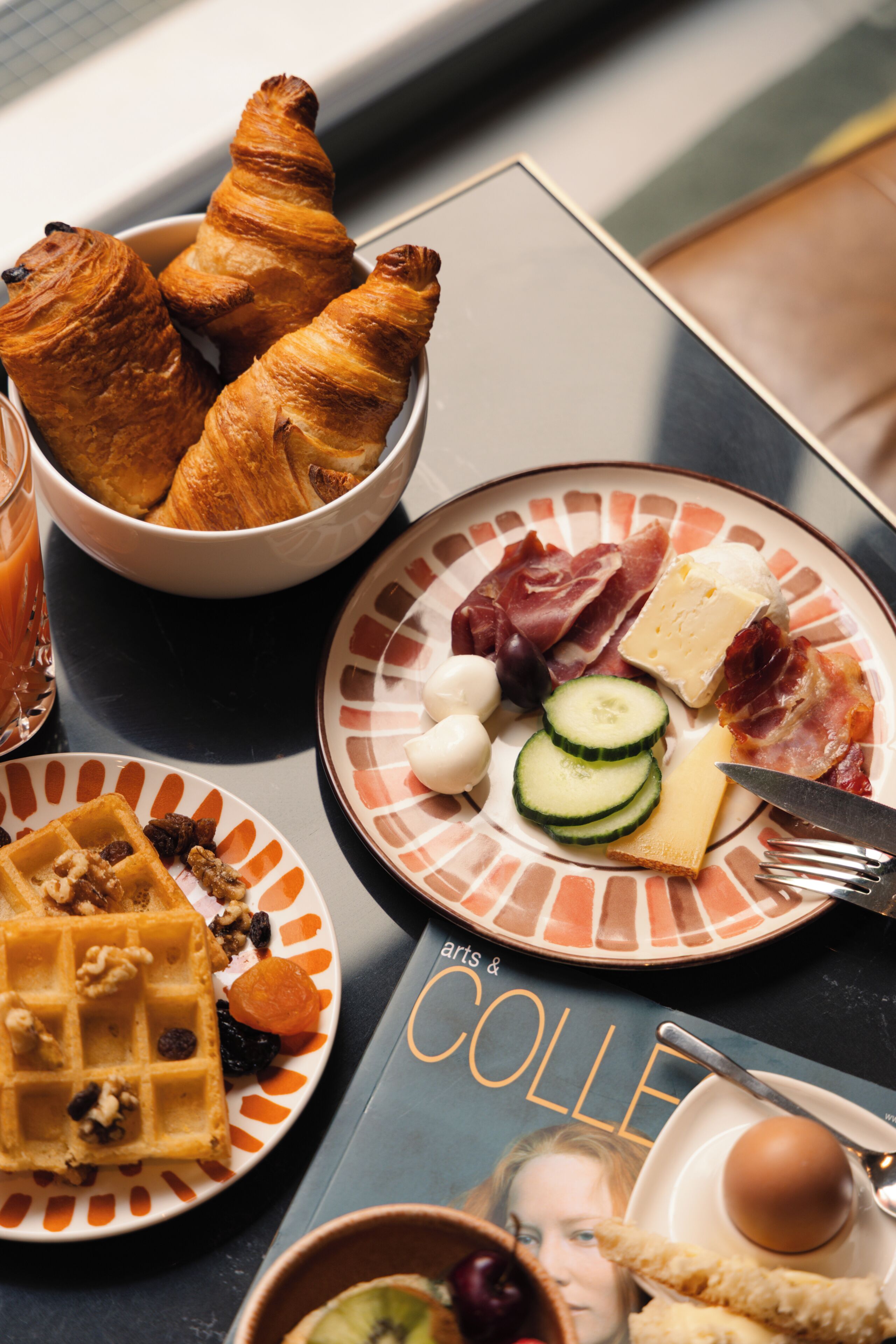 Ein Frühstückstisch mit Croissants, Käse, Wurstwaren und einem Waffel.