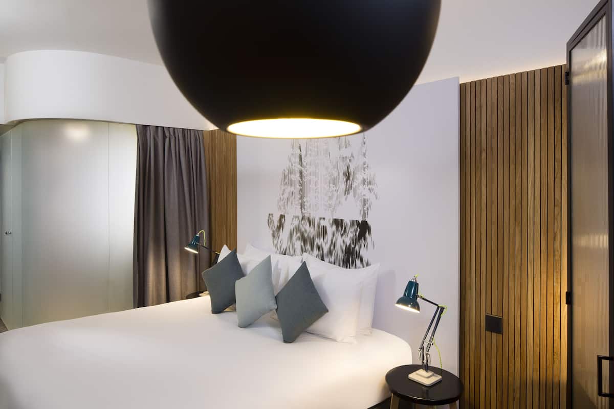 A modern hotel room with a large bed, a desk, and a large wall-mounted light fixture.