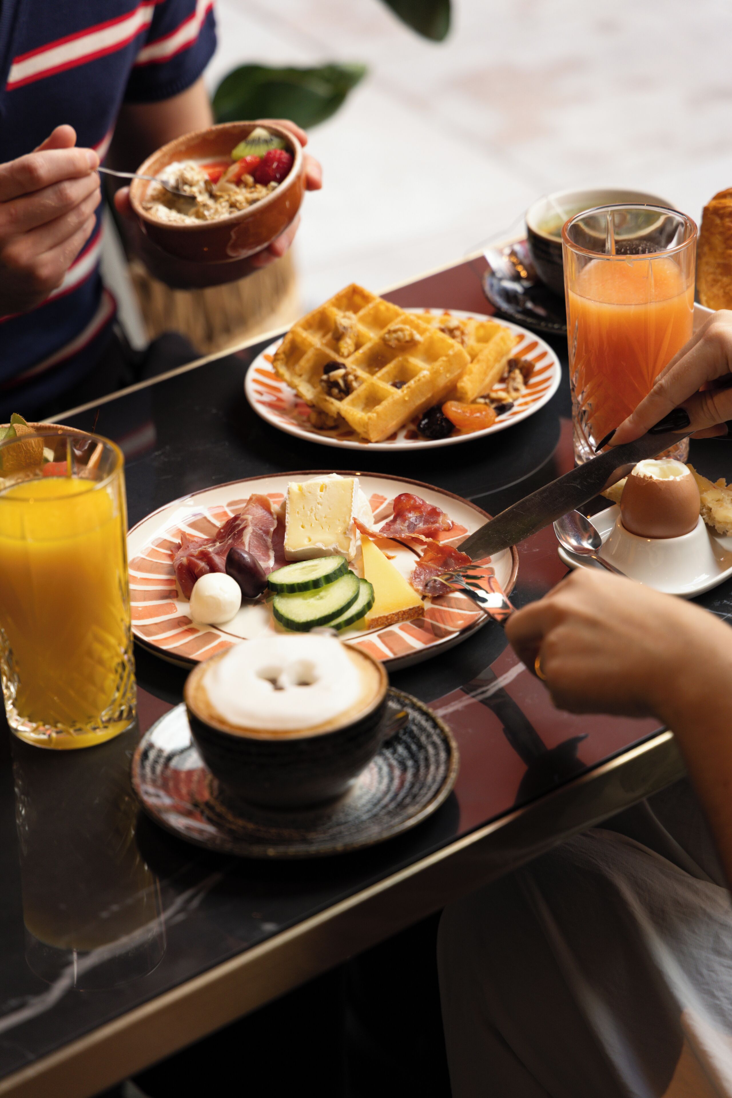 Desayuno con platos de comida, un vaso de jugo de naranja y un waffle.