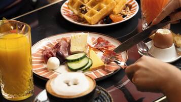 Desayuno con platos de comida, un vaso de jugo de naranja y un waffle.