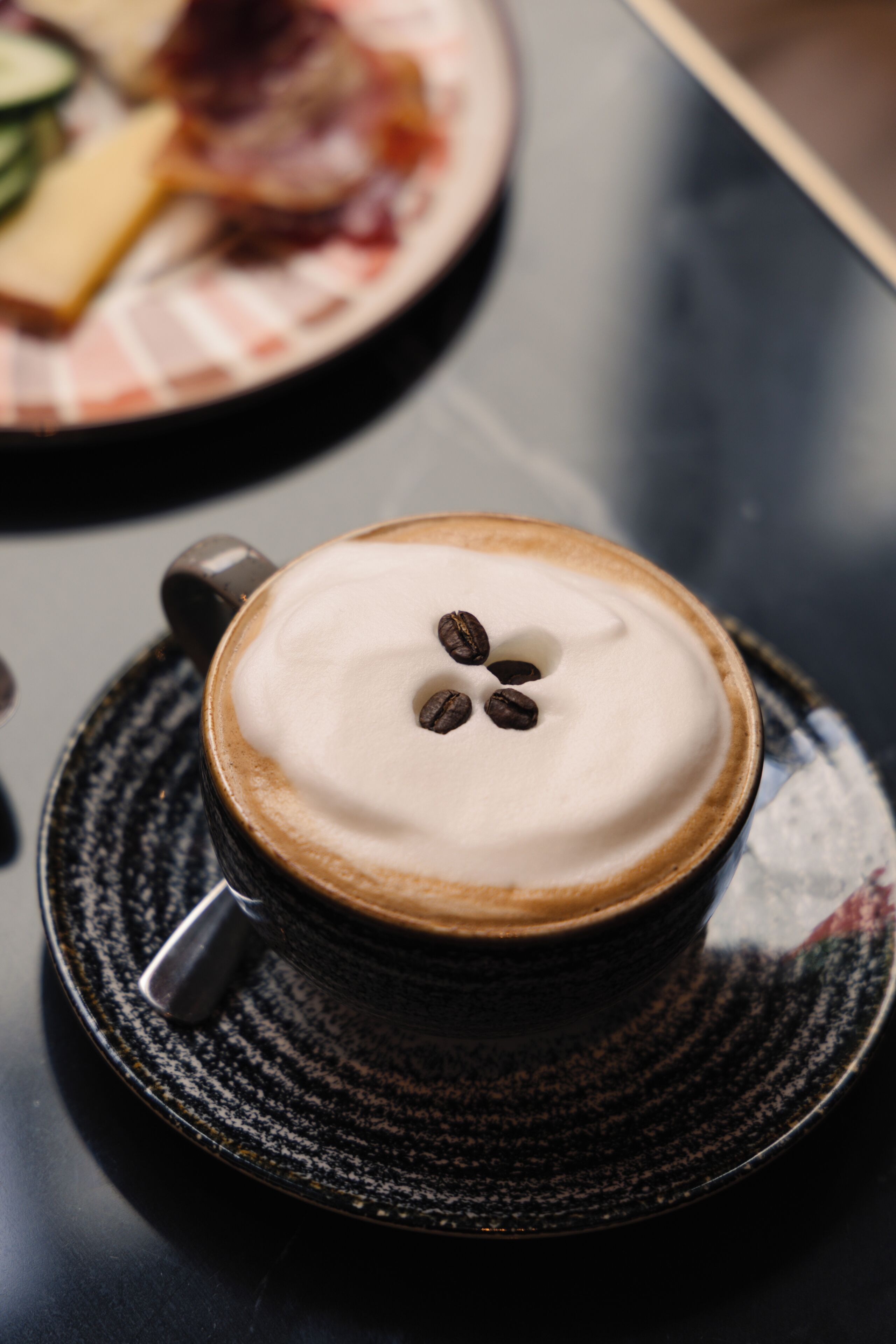 Una taza de café con espuma y granos de café sobre un platito.