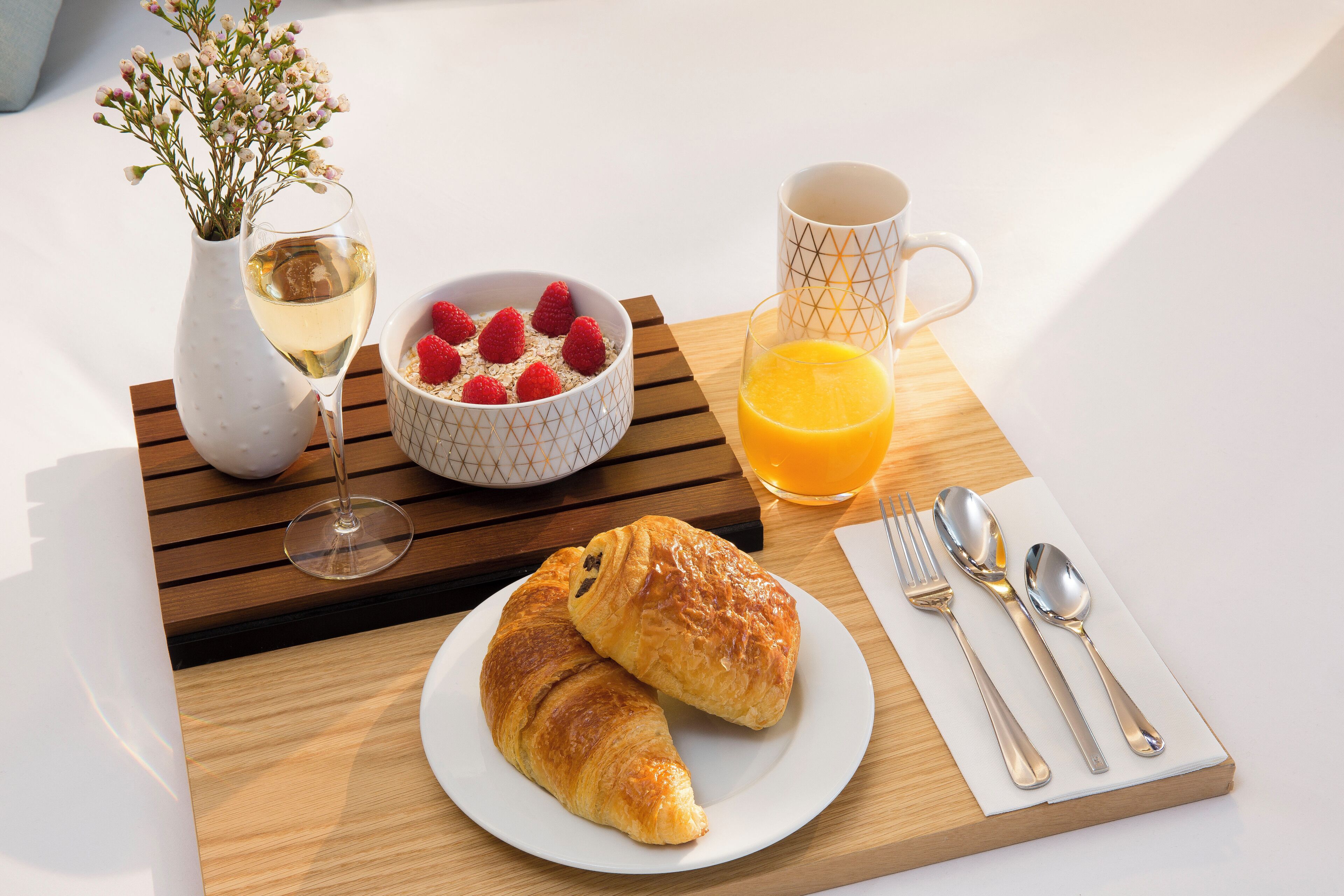 Une table mise pour le petit-déjeuner avec des croissants, un bol de fraises, un verre de jus d’orange, une tasse de café et un vase de fleurs.
