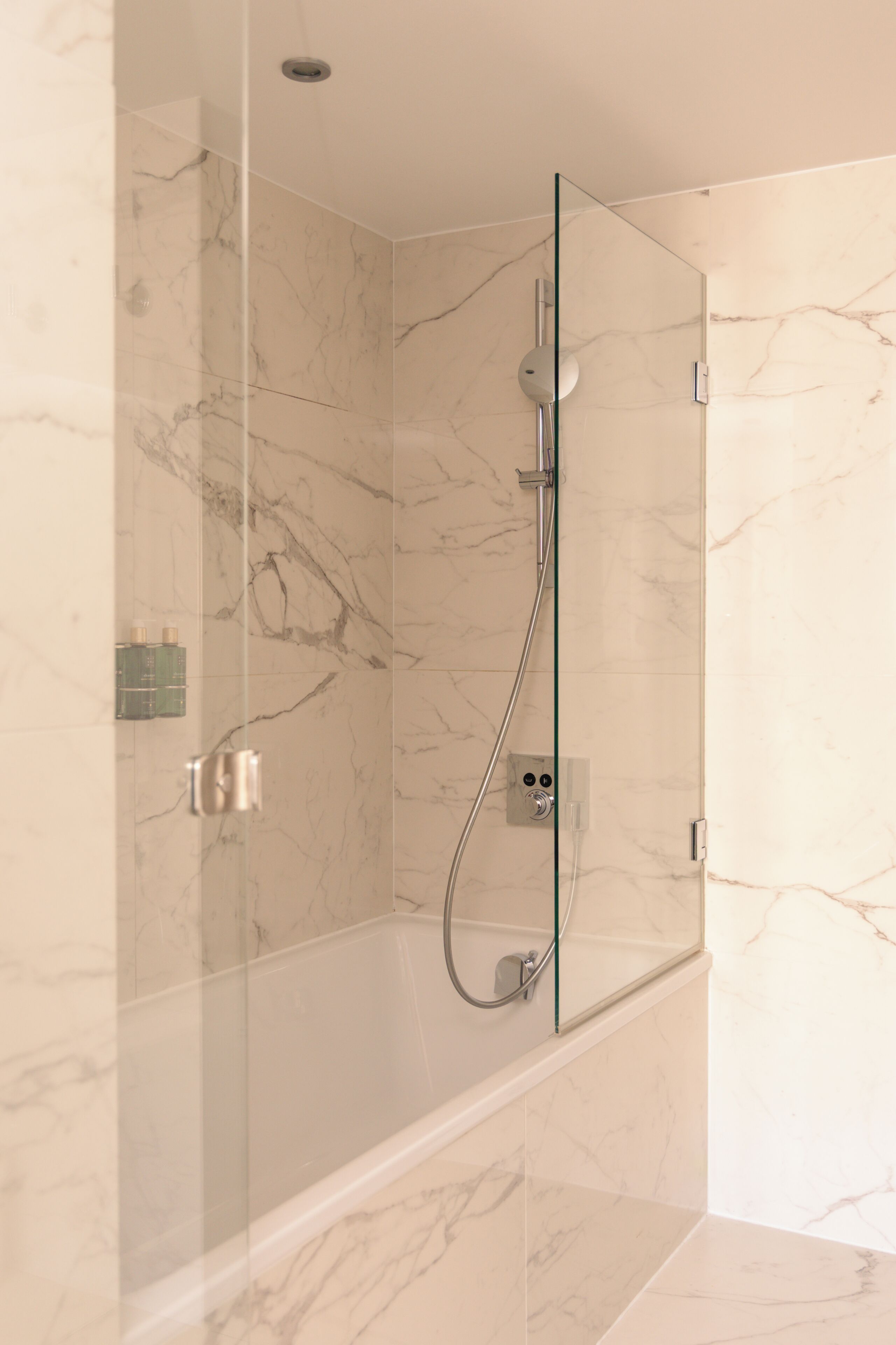 A modern shower with a glass door, marble walls, and a sleek faucet.