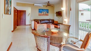 Sala de estar com mesa de jantar de vidro, cadeiras de vime, um sofá e um ventilador de teto.
