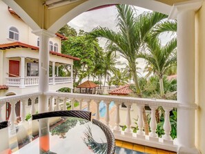 A balcony with a glass table, white balustrades, and a view of a building with a red door and a gazebo. - Jaco Beach Village 7 (Jacó)