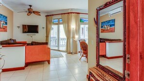 Quarto de hotel com uma cama grande, televisão, ventilador de teto, varanda com cortinas e um espelho amplo.
