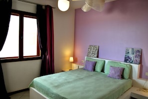 A bedroom with a bed, a nightstand, a lamp, and a window with curtains. - Sea View Apartments Boa Vista (Boa Vista)