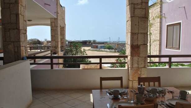 A balcony with a dining table set for four, overlooking a residential area with houses and a clear sky. - Sea View Apartments Boa Vista (Boa Vista)