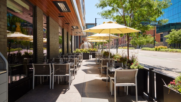 An outdoor cafe with tables and chairs, umbrellas, and potted plants. - Limelight Hotel Denver (Denver)