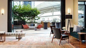 A modern lounge area with a large window, a green sofa, a red chair, and a wooden coffee table. - Limelight Hotel Denver (Denver)