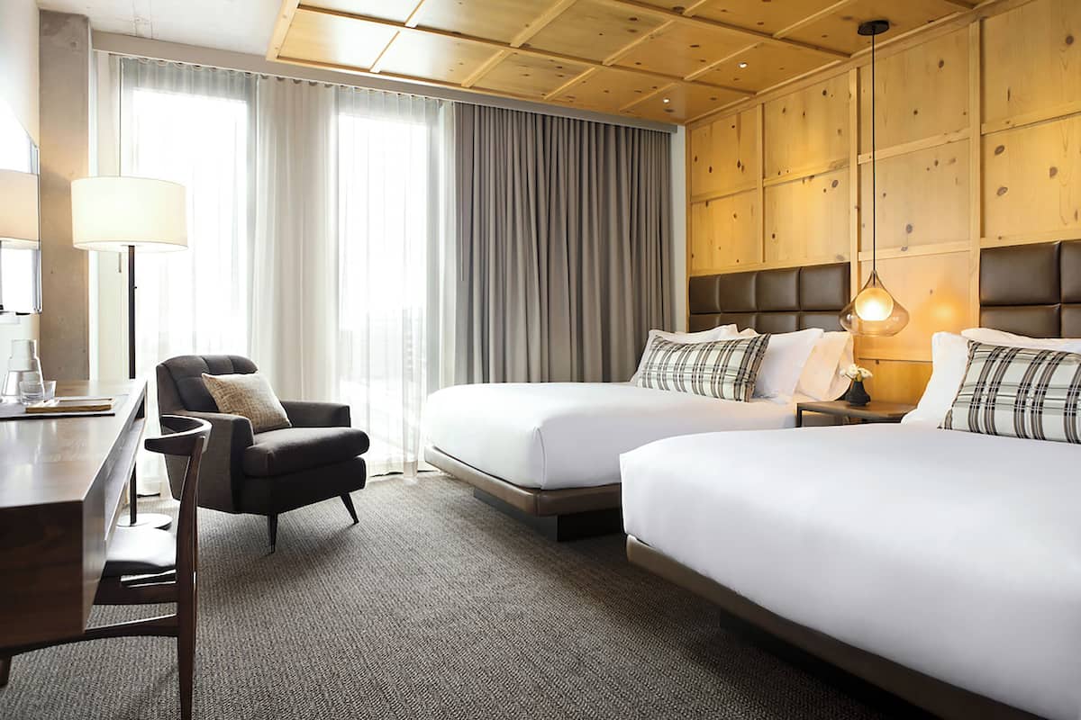 A hotel room with two beds, a desk, a chair, and a large window with curtains.