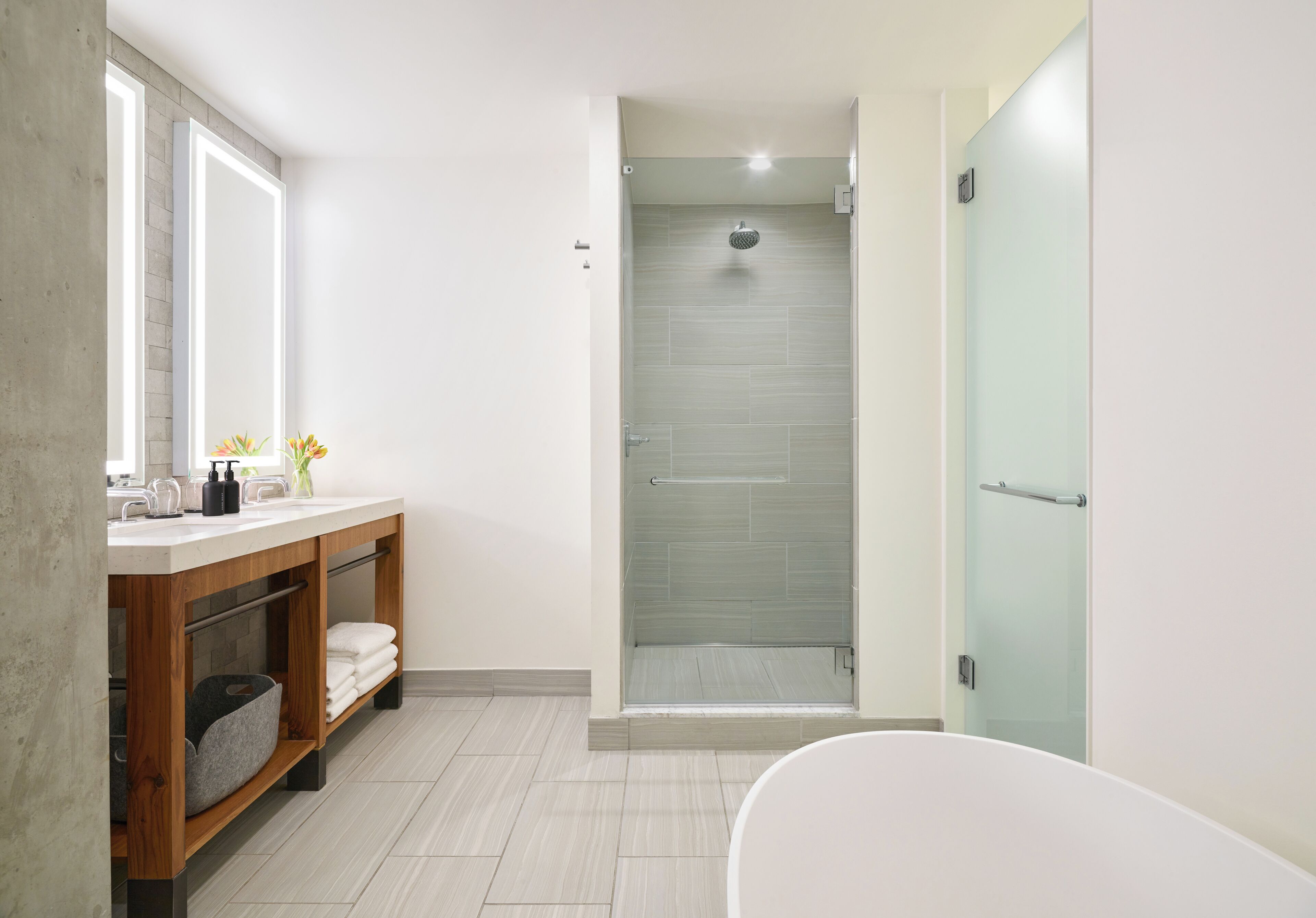 A modern bathroom with a glass-enclosed shower, a wooden vanity with a mirror, and a freestanding bathtub.