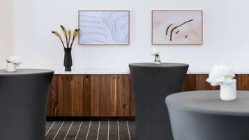 A modern reception area with a wooden panel wall, two framed abstract paintings, and three round tables with white flowers.