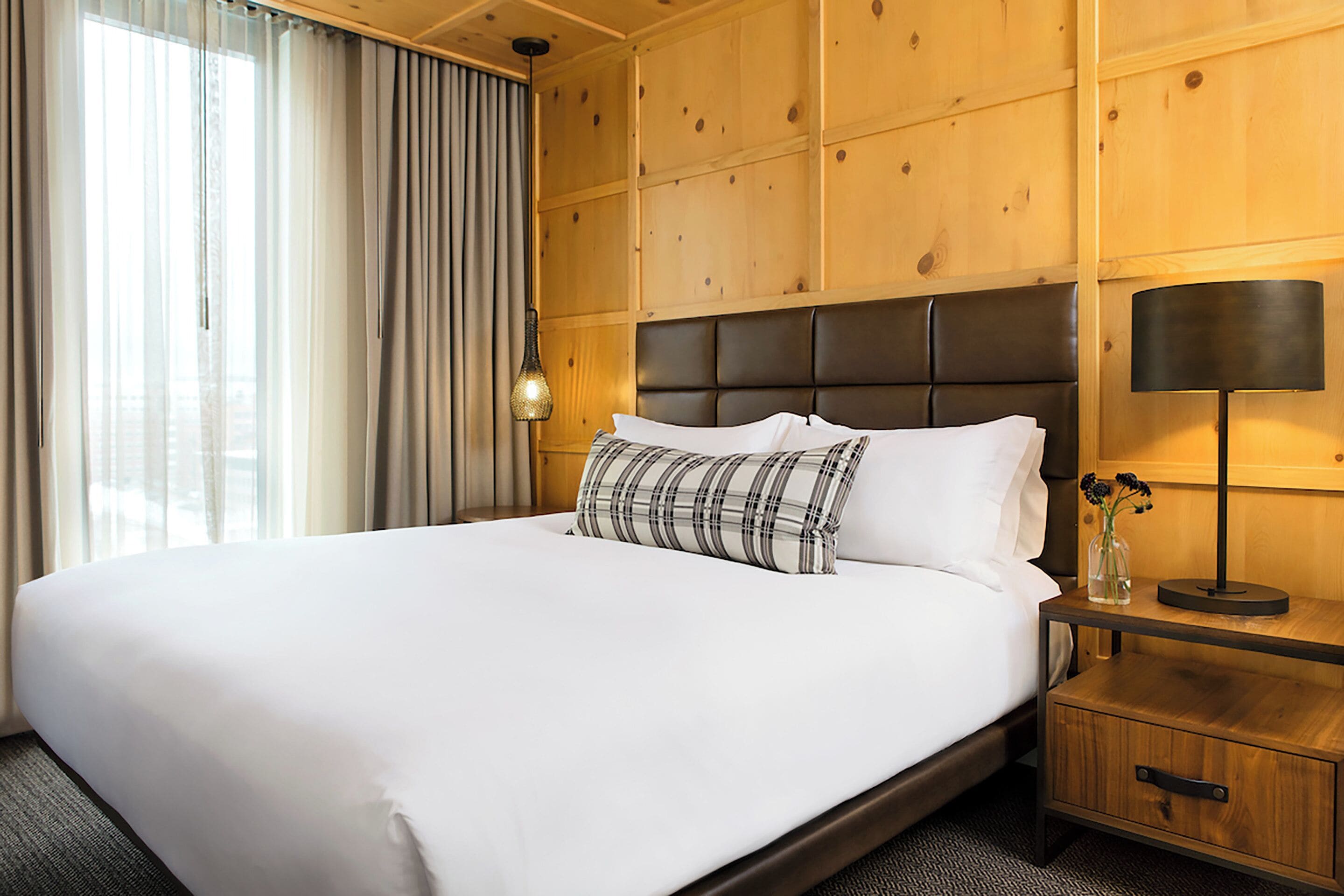 Una habitación de hotel con una cama grande, paneles de madera, una mesita de noche y una lámpara.