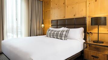 Una habitación de hotel con una cama grande, paneles de madera, una mesita de noche y una lámpara.