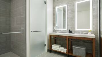 Un baño moderno con cabina de ducha de vidrio, tocador de madera con espejo y un perchero para toallas.
