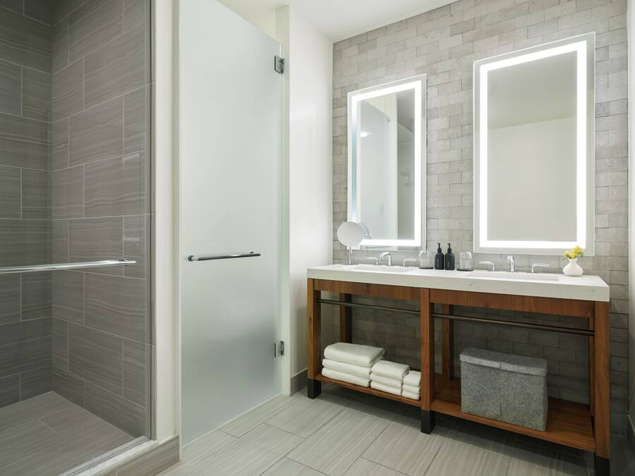 Un baño moderno con cabina de ducha de vidrio, tocador de madera con espejo y un perchero para toallas.