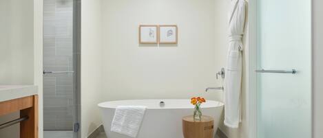 Ein modernes Badezimmer mit freistehender Badewanne, einer Duschkabine aus Glas und einem Holztischchen mit Blumen.'