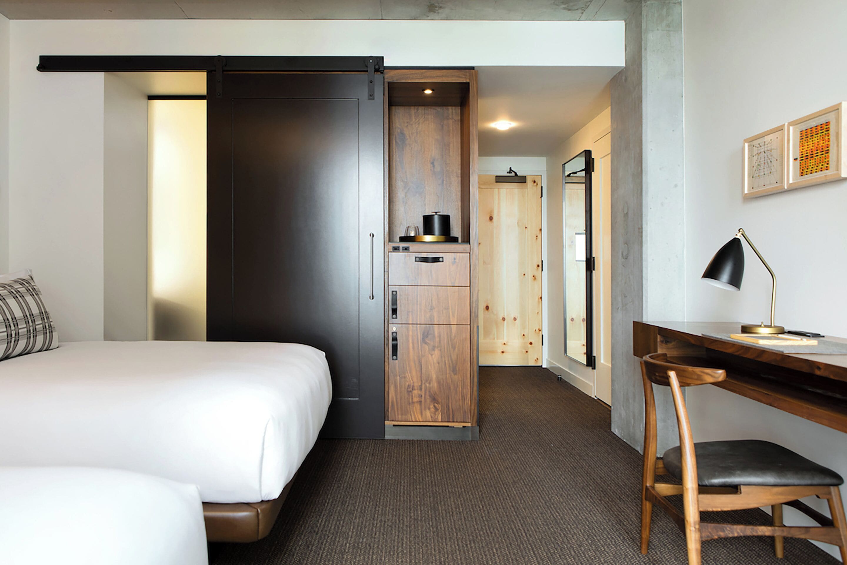 A hotel room with a bed, a desk, a chair, a wardrobe, and a small kitchenette.