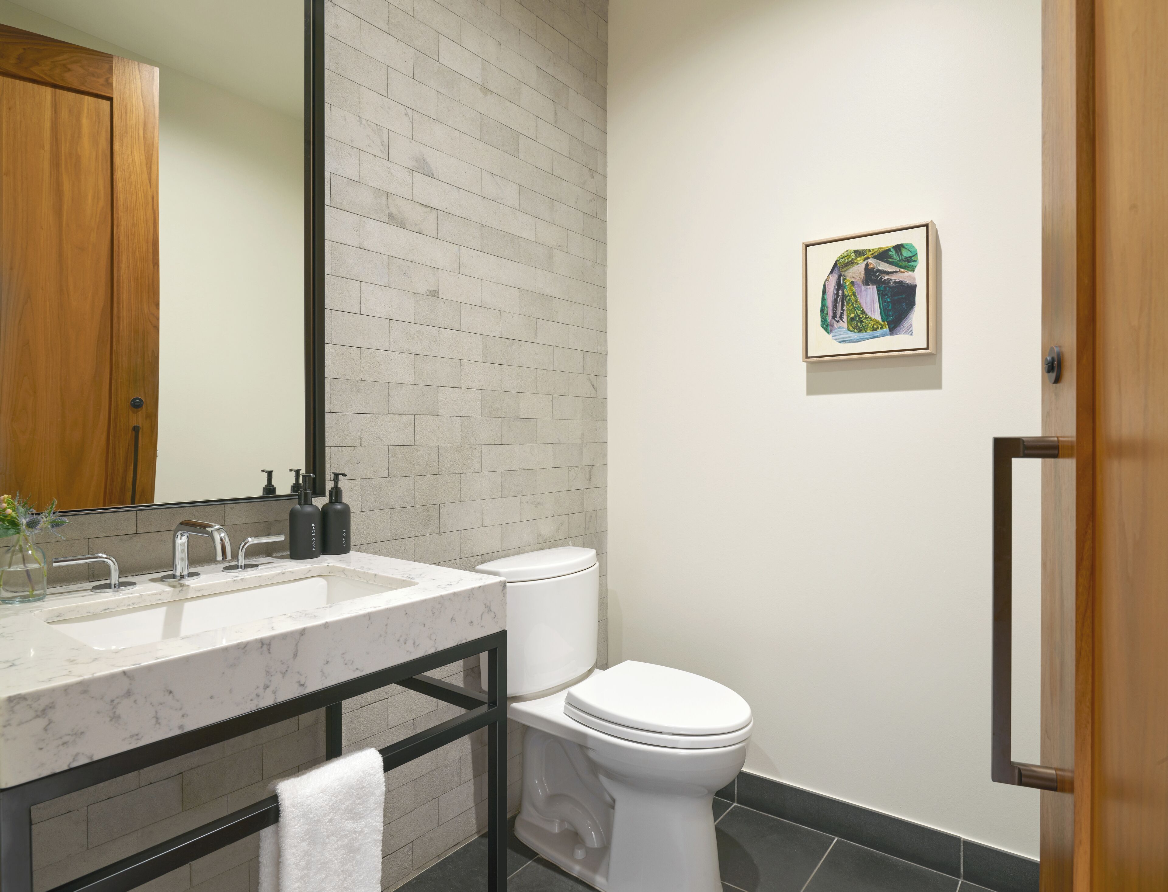 A modern bathroom with a marble sink, a toilet, and a framed artwork on the wall.