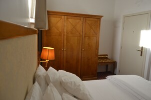 A hotel room with a bed, a wooden wardrobe, a lamp, and a bench.