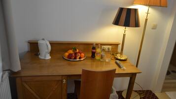 Un escritorio de madera con una bandeja de fruta, una tetera y botellas. Hay una lámpara con una pantalla a rayas y una silla frente al escritorio.