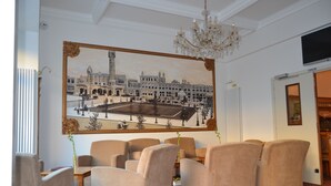 Ein geräumiges Zimmer mit einem großen Gemälde eines historischen Gebäudes, bequemen Sitzgelegenheiten und einer Kristallleuchter.