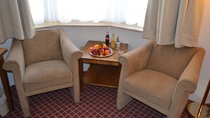 Ein Zimmer mit zwei beigen Sesseln, einem kleinen Holztisch mit Obstschale, zwei Flaschen und einem Glas.
