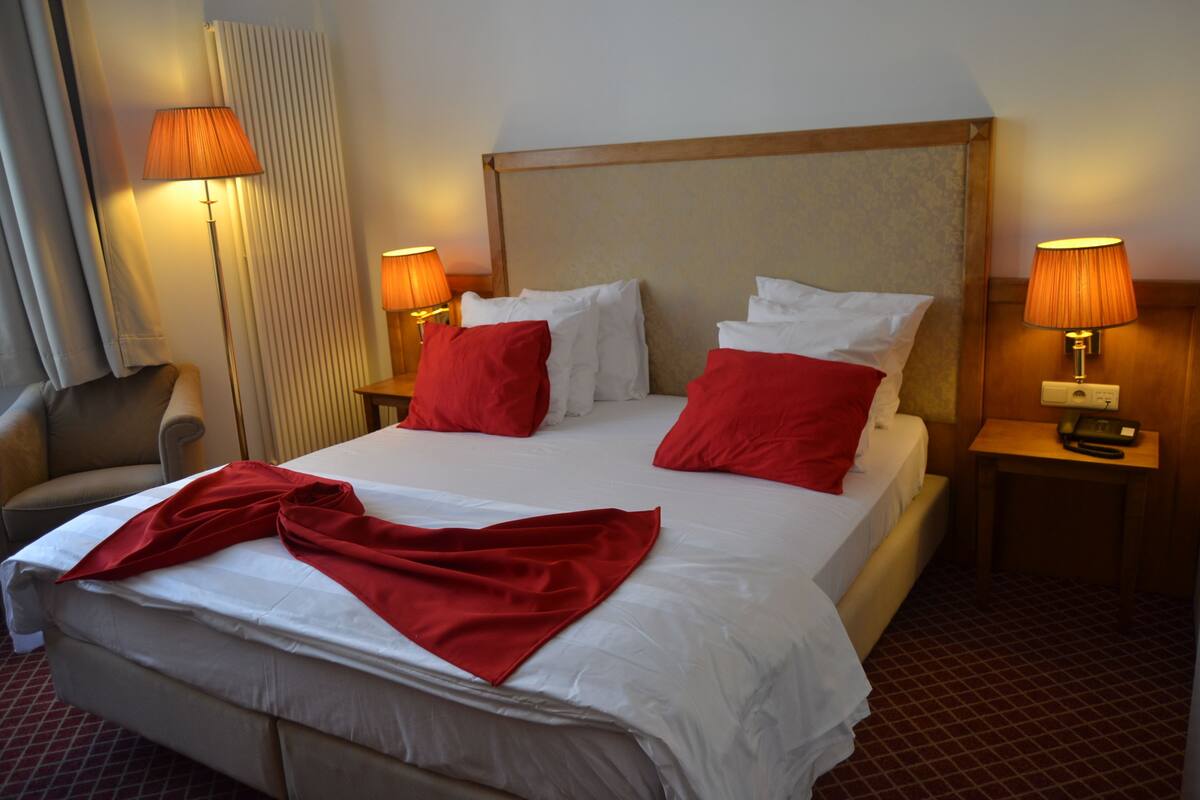 Een hotelkamer met een groot bed, twee nachtkastjes met lampen, een stoel en een radiator.