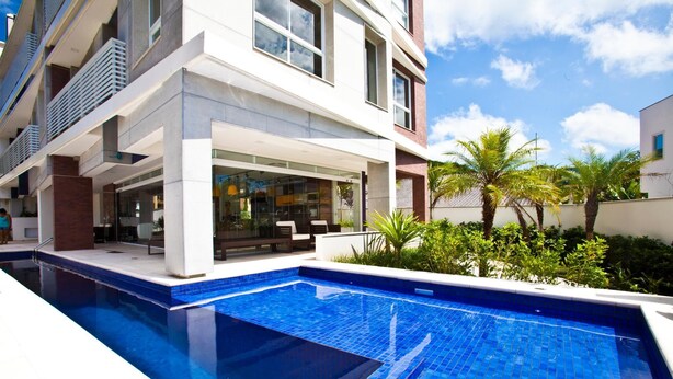 A modern building with a swimming pool and outdoor seating area. - FL002 2 Bedroom Apartment By Senstay (Florianópolis)