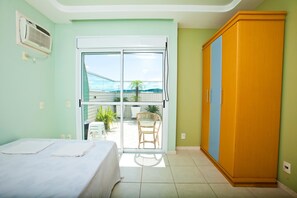 A room with a bed, a wardrobe, and a sliding glass door leading to a balcony with plants and a chair.