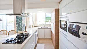 A modern kitchen with a gas stove, microwave, and sink. - FL014 3 Bedroom Apartment By Senstay (Florianópolis)