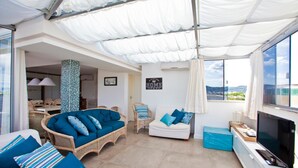 A spacious living area with a large window, a white sofa, a wicker armchair, and a television. - FL014 3 Bedroom Apartment By Senstay (Florianópolis)