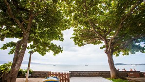 A beachside view with a boat, trees, and a calm sea. - FL023 6 Bedroom Holiday home By Senstay (Florianópolis)