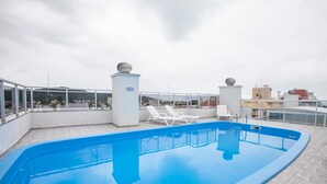 A rooftop swimming pool with clear blue water, white lounge chairs, and a glass balustrade.
