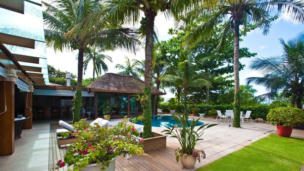 A pool area with lounge chairs, a thatched-roof structure, and lush greenery. - FL004 5 Bedroom Villa By Senstay (Florianópolis)