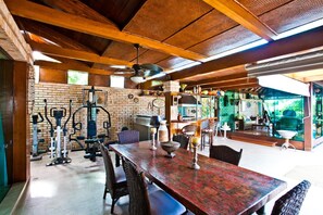 Un'ampia area interna con un grande tavolo di legno, attrezzature per l'esercizio fisico e una zona pranzo con sedie e tavolo.