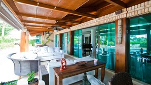 A covered outdoor seating area with wicker furniture, a wooden table, and a piano in the background. - FL004 5 Bedroom Villa By Senstay (Florianópolis)