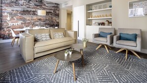 Ein modernes Wohnzimmer mit Stadtbild-Wandgemälde, einem beigen Sofa, zwei Sesseln, einem Couchtisch und einem gemusterten Teppich.