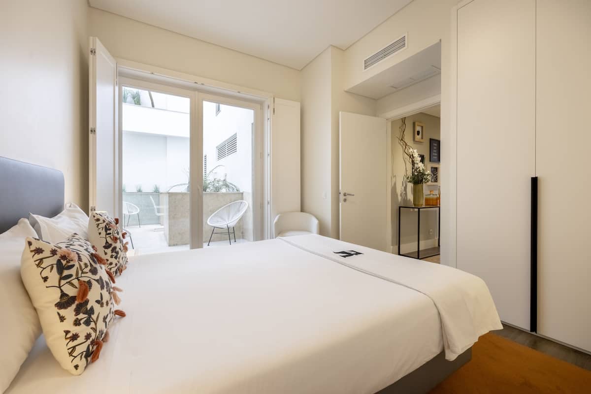 Ein Schlafzimmer mit Bett, einem Sessel und einer Tür zu einem Außenbereich.