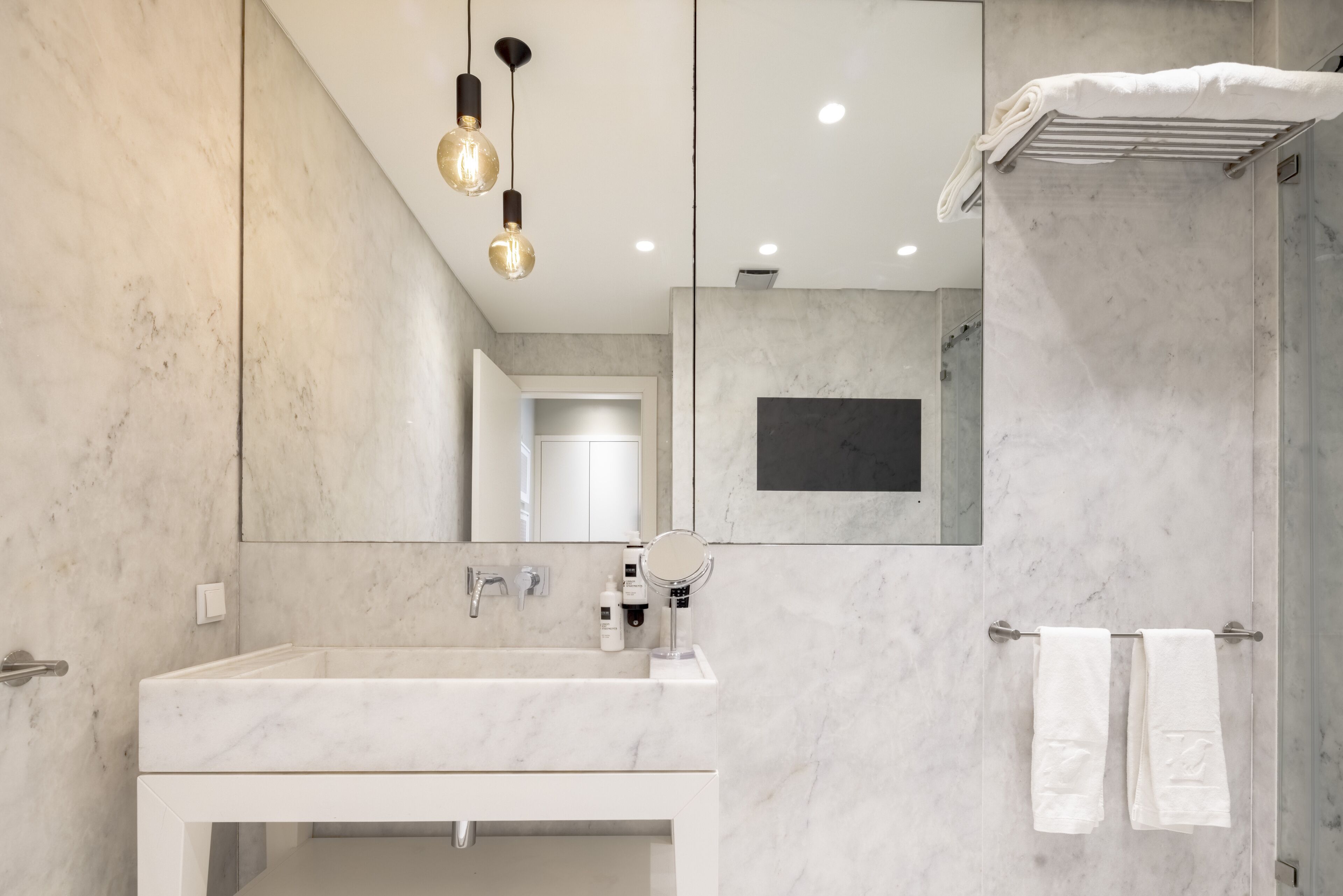 A modern bathroom with a marble sink, a mirror, and a towel rack.