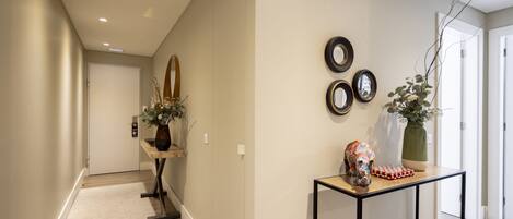 A hallway with a wooden floor, a small table with a vase and a decorative item, and three framed mirrors on the wall.