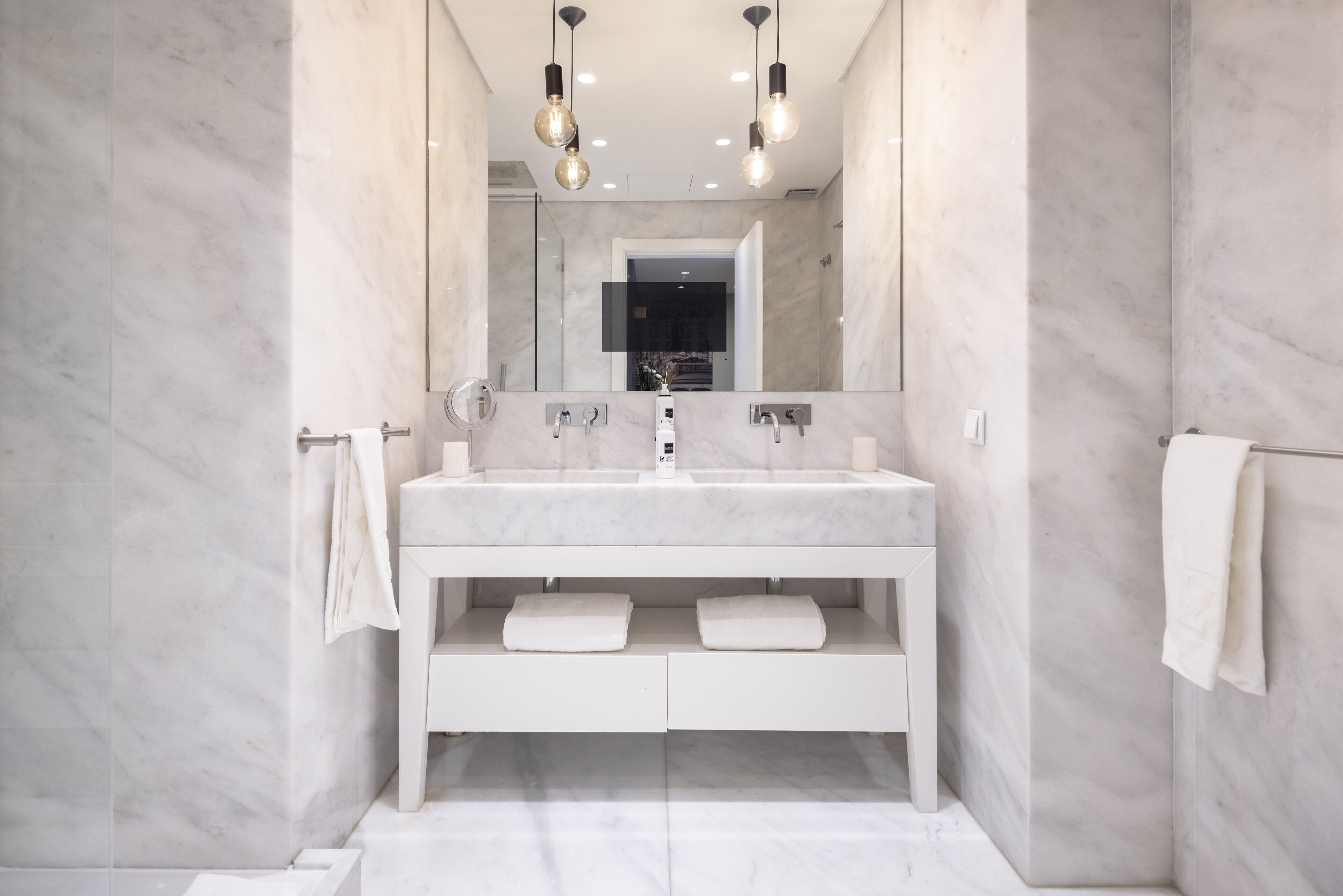 Un baño moderno con tocador blanco, dos lavamanos y un espejo grande.