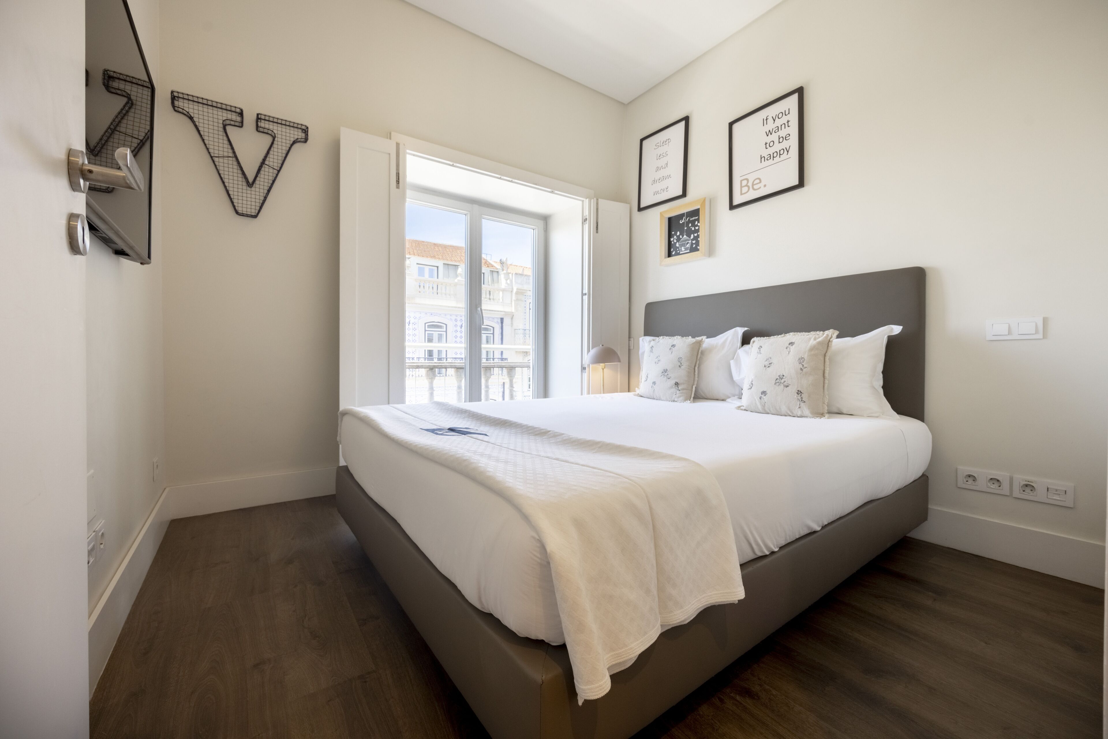 Un dormitorio con una cama grande, una ventana que ofrece vistas a edificios y una pared decorada con cuadros.