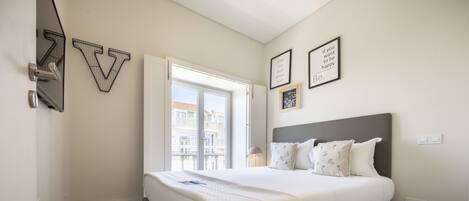 Un dormitorio con una cama grande, una ventana que ofrece vistas a edificios y una pared decorada con cuadros.