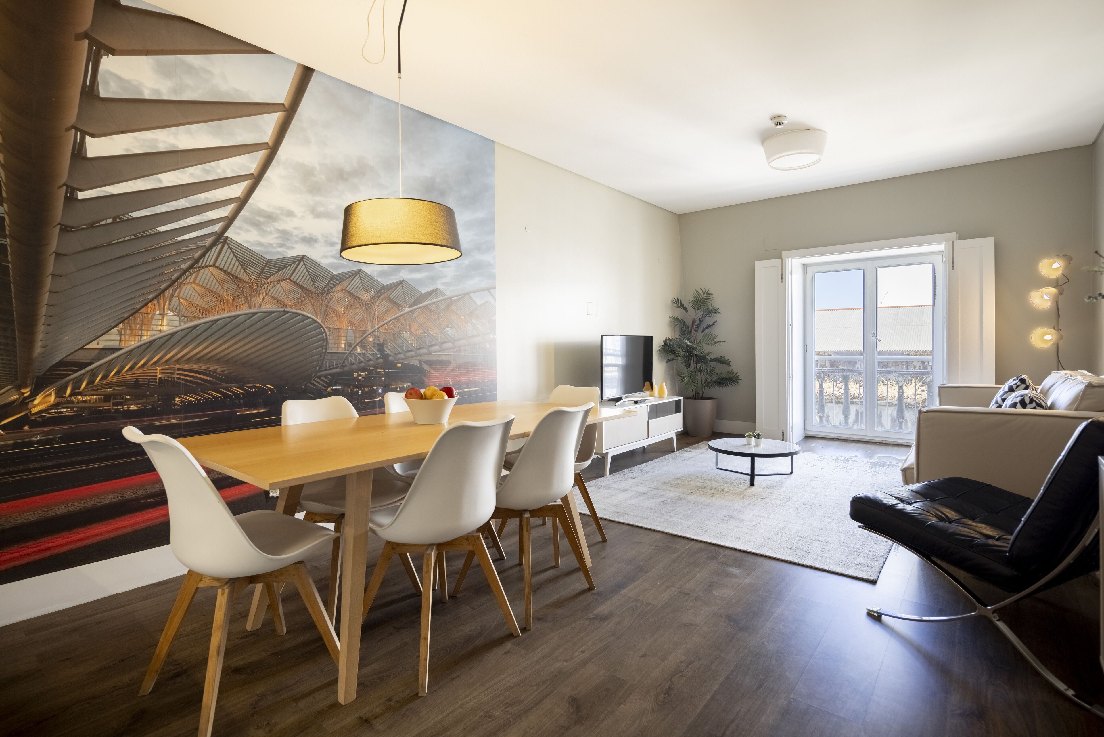 A modern living room with a dining area, a staircase, and a large window.