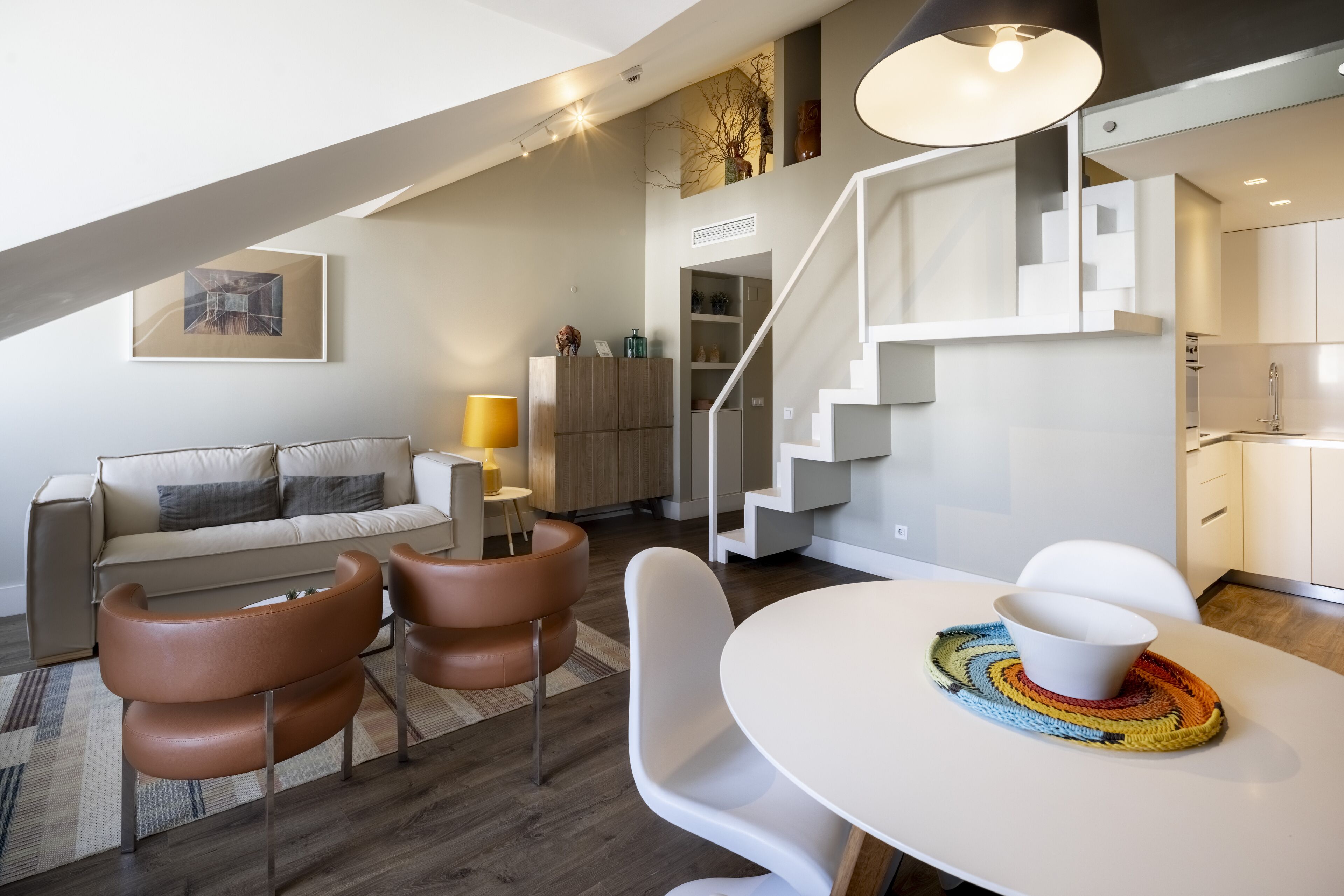 Ein modernes Wohnzimmer mit einer Couch, Sesseln, einem Esstisch und einer Treppe.